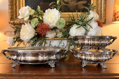 deux plats en argent posés sur une table, avec des fleurs en arrière-plan