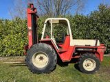 a red forklift parked in the grass in front of a hedge