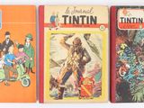 three books are lined up on a white surface one is a tintin and the other is a tintin