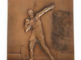 bronze plaque of a man throwing a ball on a tennis court