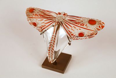 Sculpture de papillon en verre orange et blanc, posée sur un socle, sur fond blanc