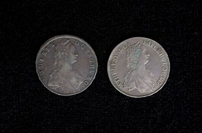 two silver coins on a black surface with one of them facing the camera