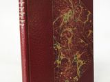 an old book with a red cover sitting on top of a white table