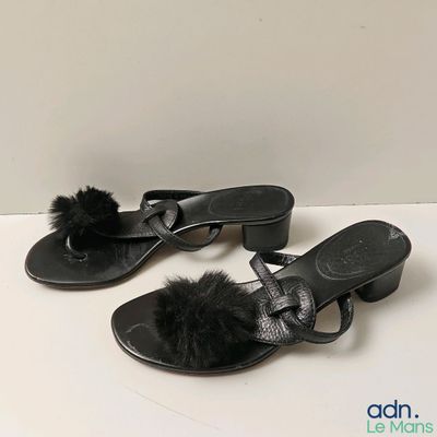 pair of black sandals with pom poms on them sitting on a white surface