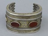 silver cuff bracelet with red stones on it on a white surface
