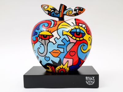 une sculpture de pomme aux couleurs vives posée sur un socle noir, sur fond blanc