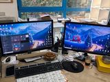 two computer monitors sitting on a desk in front of a window