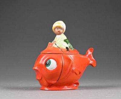 a figurine of a boy sitting on top of a fish shaped teapot