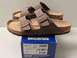 des sandales Birkenstock marron posées sur une boîte, sur une surface blanche