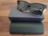 Lunettes de soleil Prada dans leur boîte et leur étui, posées sur une table en bois