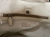 white leather handbag with zippers on top of it sitting on a table