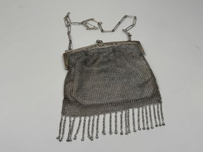 silver mesh purse with chain handles and fringes on a white surface
