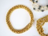 two gold and pearl necklaces and a bracelet on a white surface