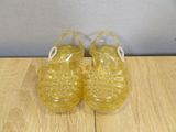 yellow jelly slippers on a wooden surface with a white background