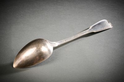 une cuillère en argent posée sur une surface grise, sur fond noir