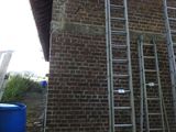several ladders are leaning against a brick wall near a blue barrel