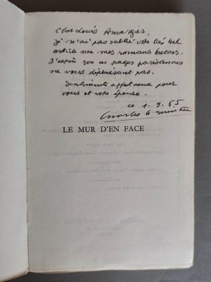un livre ouvert, sur lequel est inscrit un poème manuscrit, posé sur une table