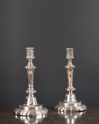 une paire de bougeoirs en argent posés sur une table, sur fond gris