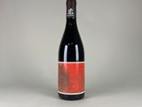 the bottle of red wine is sitting on a white surface