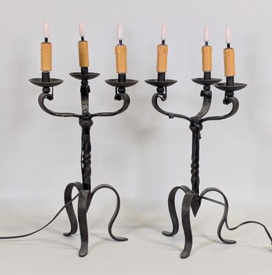 une paire de chandeliers en fer noir, chacun orné d'une bougie