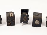 five old cameras are lined up in a row on a white surface