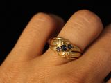 a woman ' s hand holding a gold ring with black stones