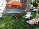 Des chaises et un parasol sont posés dans l'herbe devant une maison