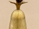 un récipient doré en forme d'ananas posé sur une surface beige