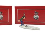 two figurines of a man on a surfboard in front of a red box