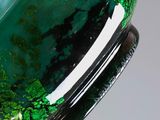 close up of a green and black glass bowl on a wooden stand