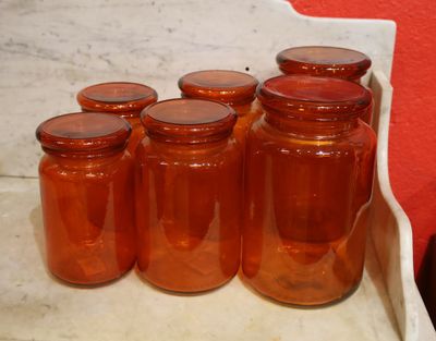several jars of orange liquid sit on a counter in front of a red wall