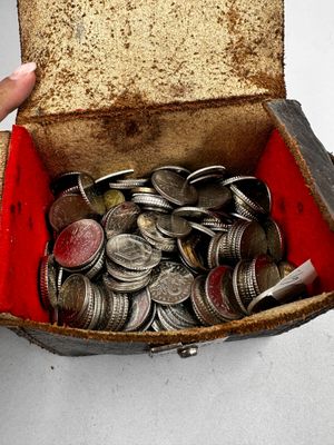 une boîte remplie de pièces argentées et rouges, vers laquelle une main se tend