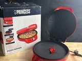 Une machine à pizza « Princess » avec sa boîte et ses ciseaux, posée sur une table en bois