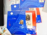 beaucoup de cartes postales posées sur la table, avec une photo de la tour Eiffel en arrière-plan