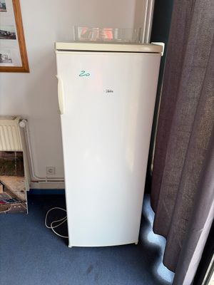 un réfrigérateur blanc près d'une fenêtre, dans une petite pièce