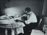 black and white photograph of a man sitting at a table writing on a piece of paper