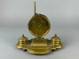 une horloge dorée posée sur un socle, sur une surface blanche