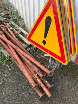 un tas de tuyaux rouillés à côté d'un panneau d'avertissement jaune et rouge