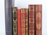 Plusieurs livres anciens sont alignés sur une étagère devant un fond blanc.