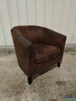 fauteuil club en cuir marron posé sur un sol en béton, devant un mur blanc