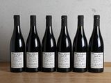six bottles of wine lined up on a table in front of a wall