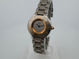 une photo d'une montre-bracelet argentée et dorée posée sur un socle blanc