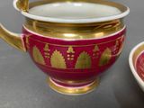 a red and gold bowl with a gold handle next to a red bowl with a gold handle