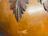 a brown vase with leaves on it sitting on a table