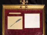 tableau dans un cadre doré représentant un stylo et un encrier sur fond noir