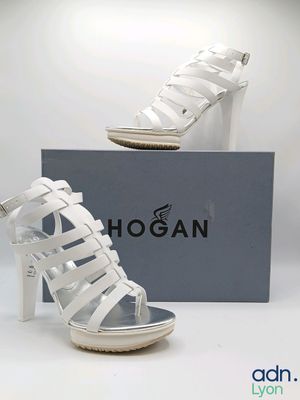 Cette chaussure est blanche, dotée d'un talon haut et d'un design en forme de cage.