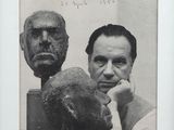 black and white photograph of a man sitting next to a bust of a man