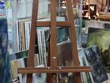 un chevalet au milieu d'une pièce, avec des tableaux posés par terre