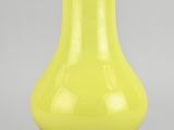 un vase jaune posé sur une surface grise, avec un arrière-plan gris