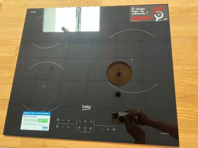 une personne tenant une télécommande devant une plaque de cuisson noire